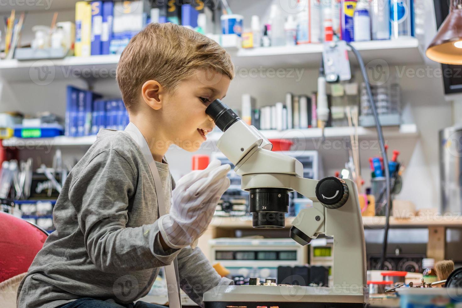 Little IT student examining circuit board through microscope. photo