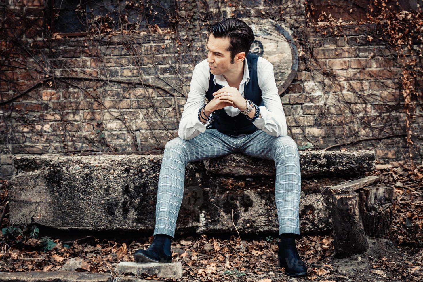 Pensive retro-styled man looking away while sitting outdoors. photo