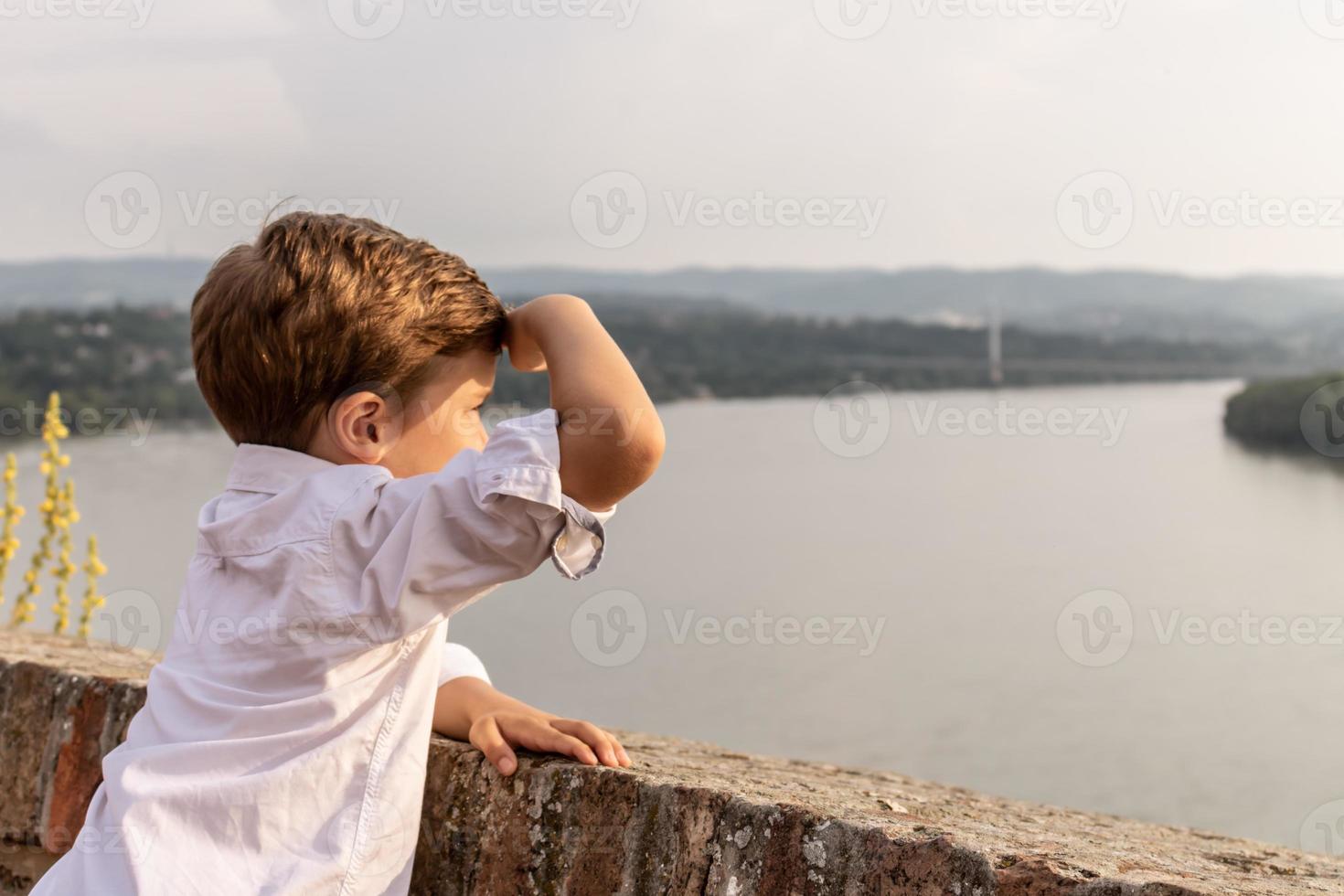 Little boy on riverside looking at the view at sunset photo