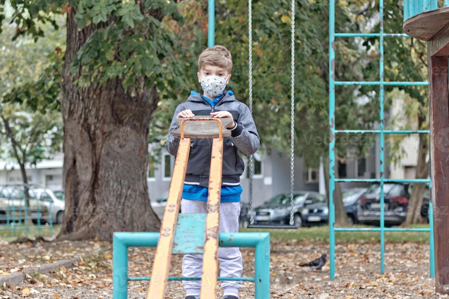 Pensive boy wearing face mask while playing alone at the playground. photo