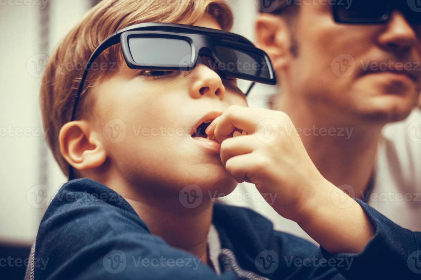 Close up of kid with 3d glasses eating popcorn photo
