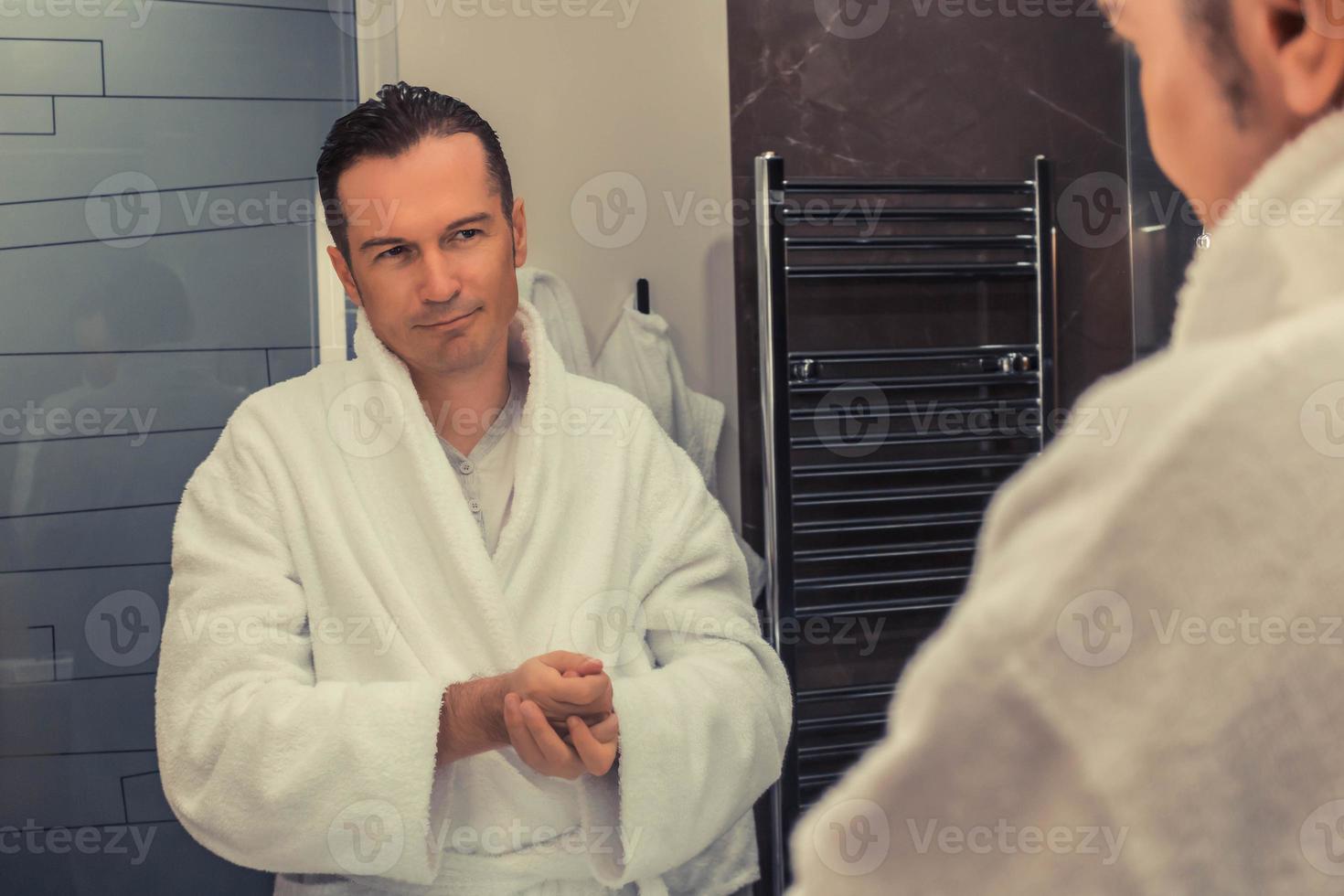 Smiling man using hand cream while looking himself in bathroom mirror ...