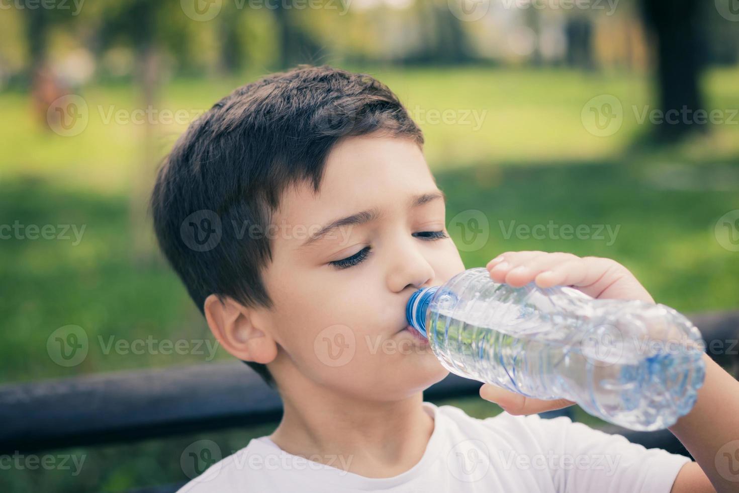 Small kid refreshing himself with water from plastic bottle. photo