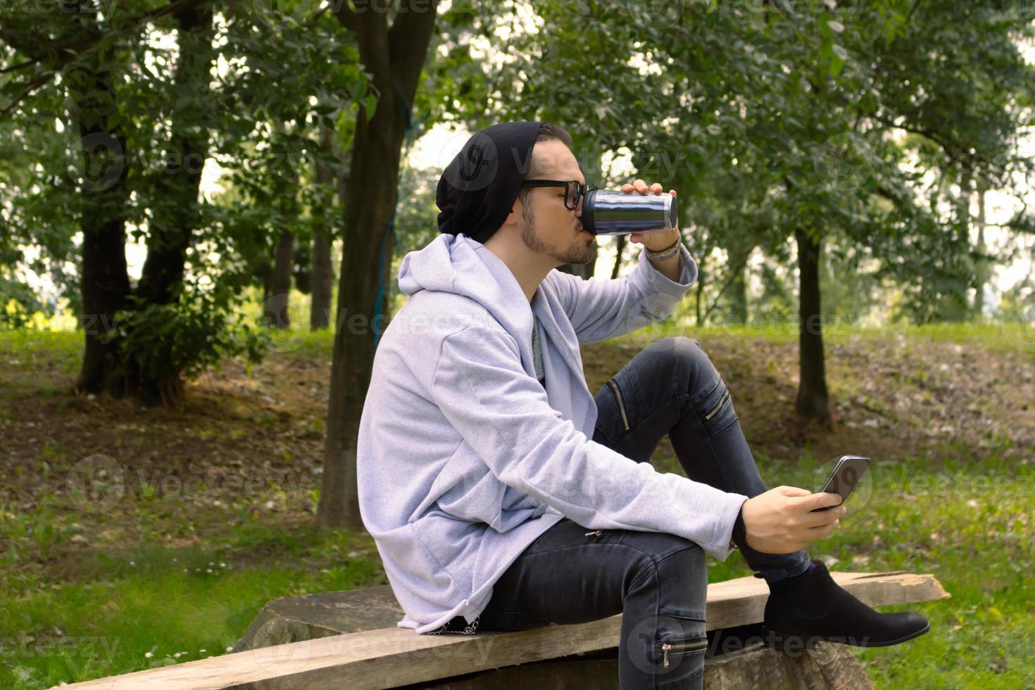 Mid adult man using mobile phone while drinking takeaway coffee in nature. photo