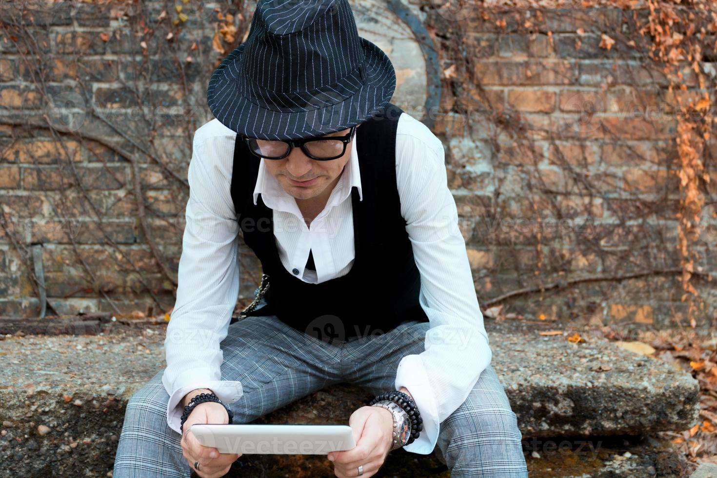 Well dressed man with fedora hat reading something on digital tablet. photo