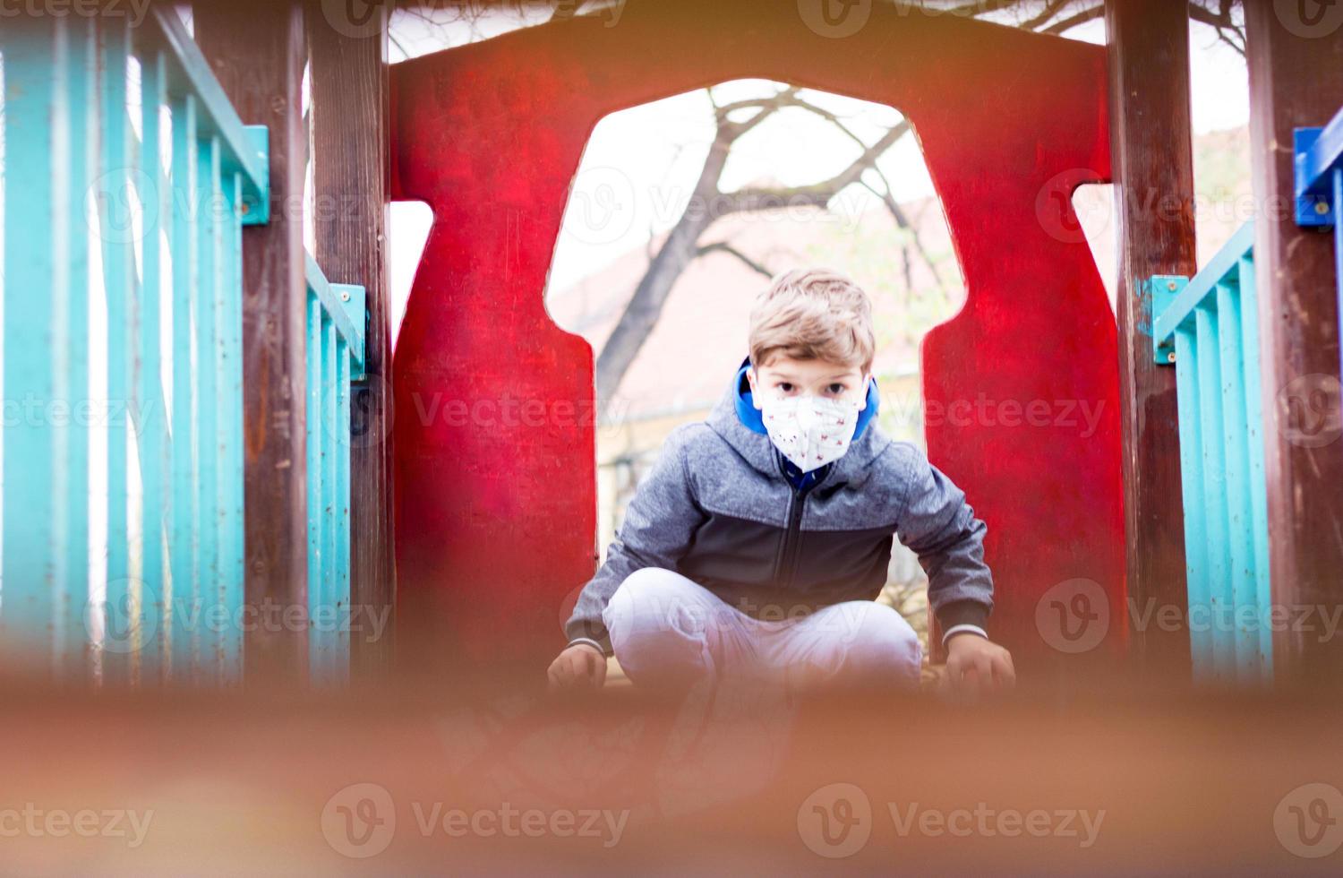 Little boy wearing face mask on the playground due to COVID-19 pandemic. photo