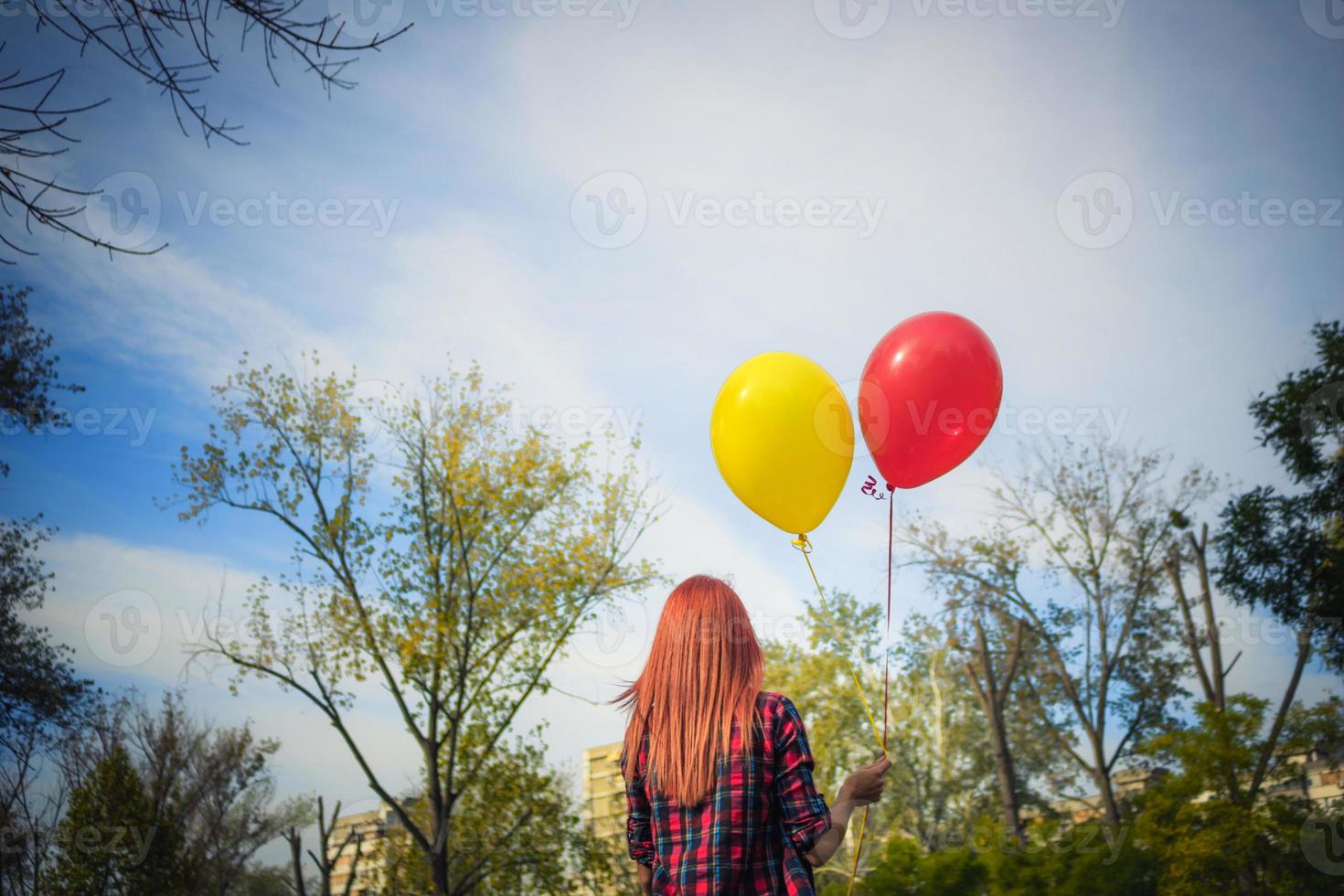 vista trasera de una mujer con globos de colores caminando por el parque. foto