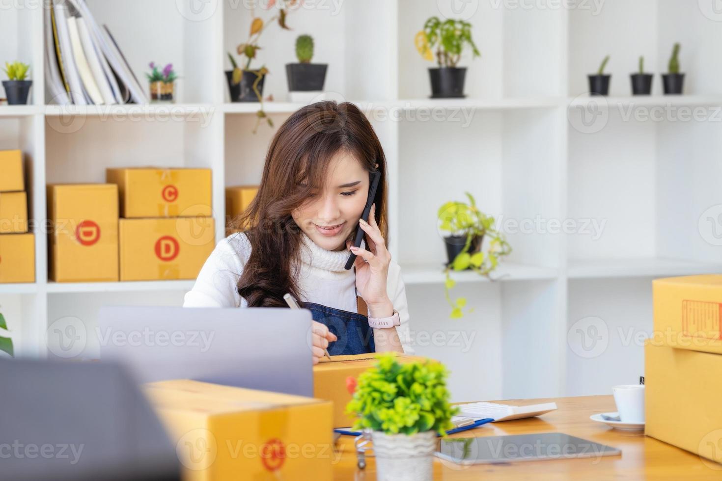 trabajar desde casa. las mujeres felices que venden productos en línea comienzan una pequeña empresa usando un teléfono inteligente y una computadora portátil para calcular los precios y prepararse para el franqueo. foto