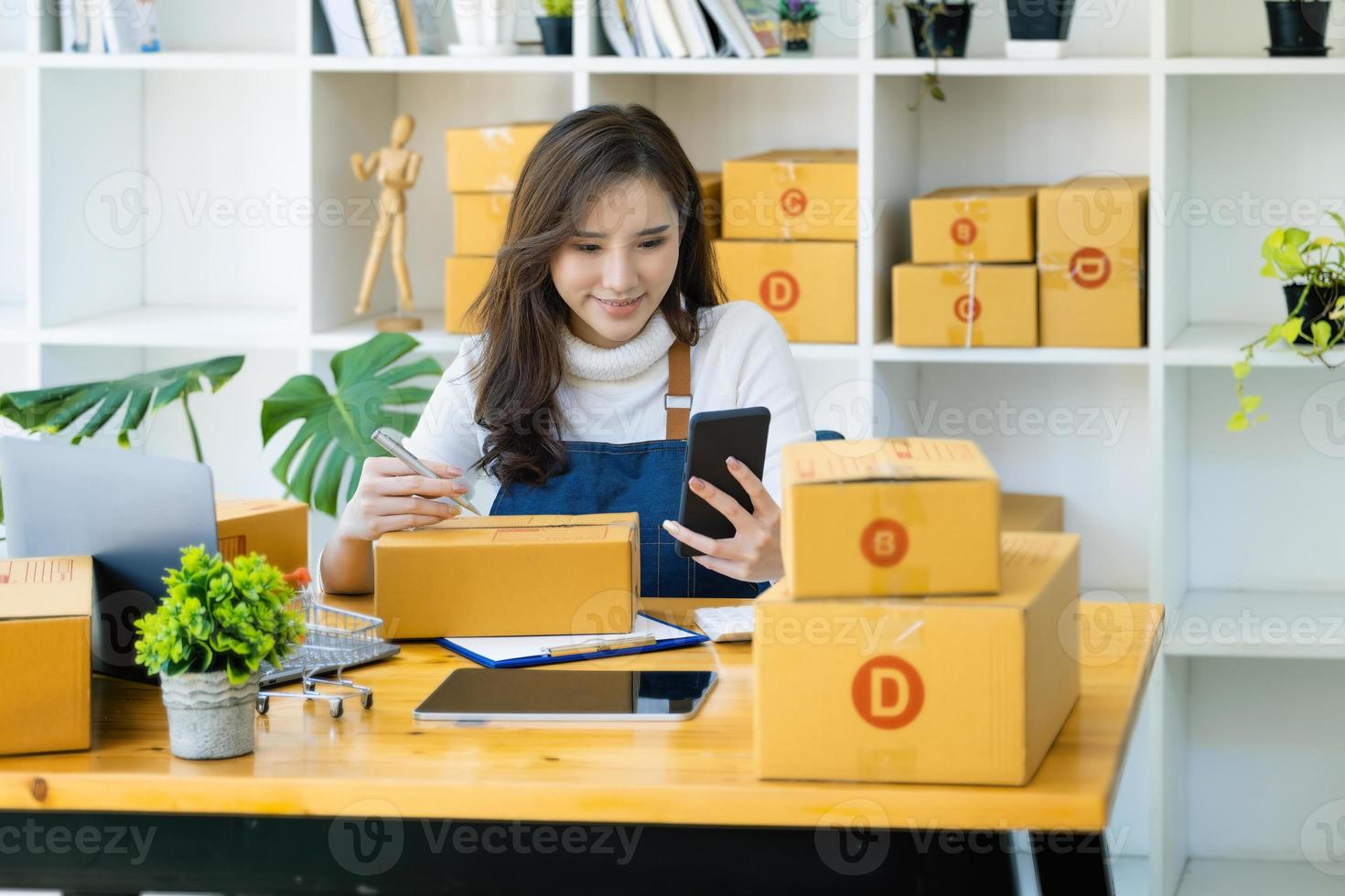 trabajar desde casa. las mujeres felices que venden productos en línea comienzan una pequeña empresa usando un teléfono inteligente y una computadora portátil para calcular los precios y prepararse para el franqueo. foto