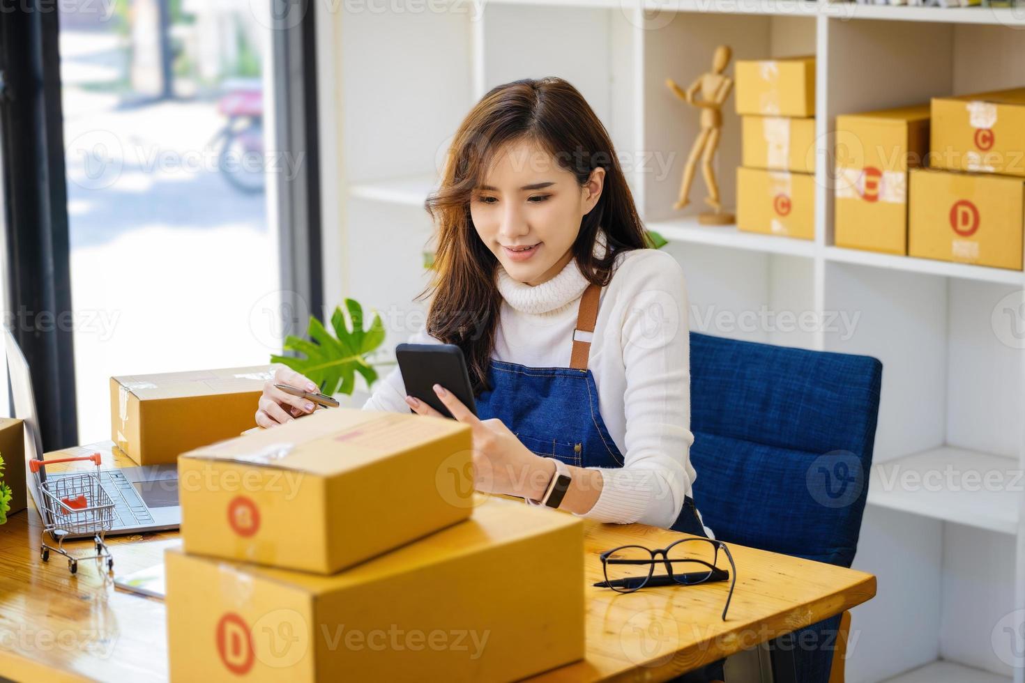 trabajar desde casa. las mujeres felices que venden productos en línea comienzan una pequeña empresa usando un teléfono inteligente y una computadora portátil para calcular los precios y prepararse para el franqueo. foto