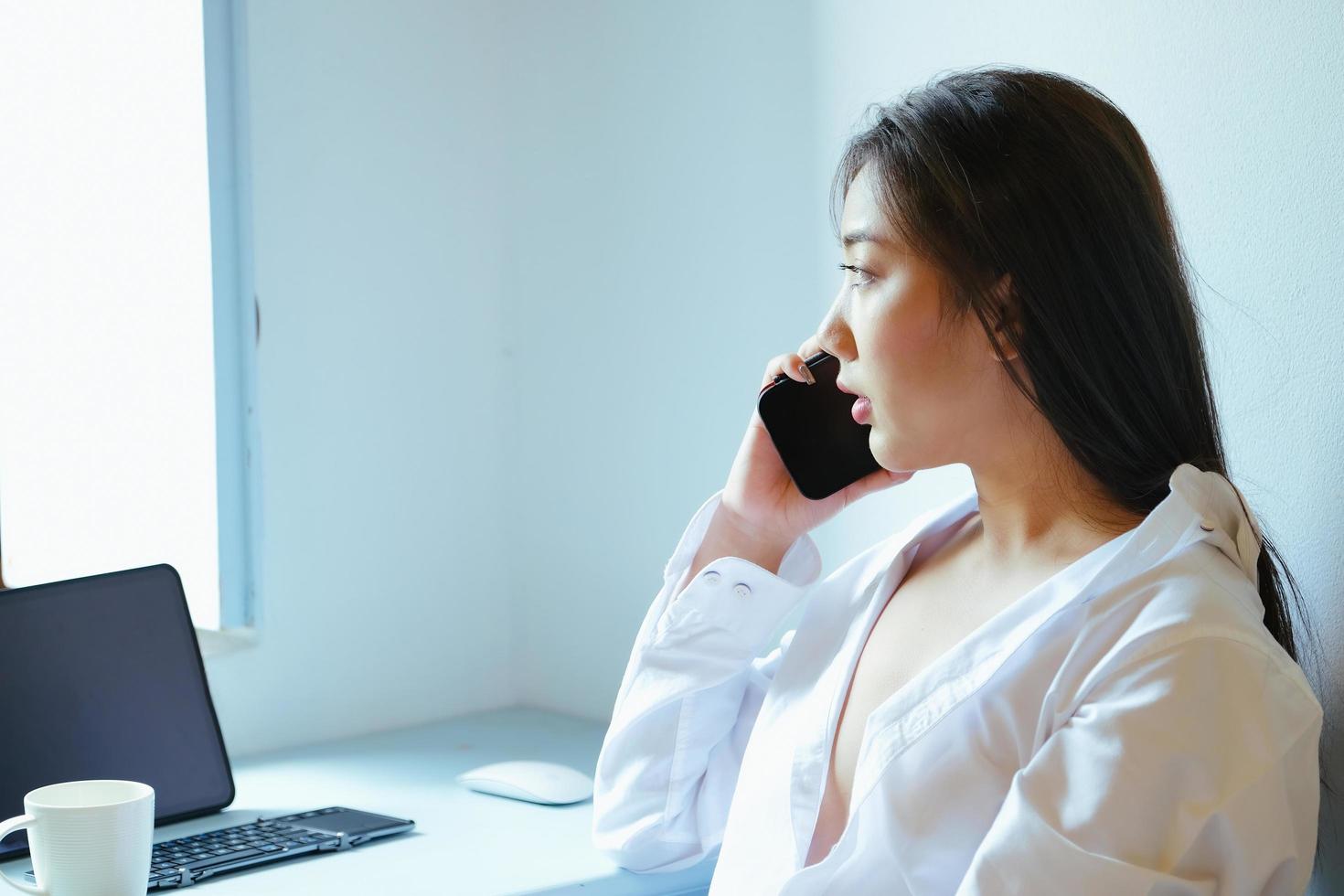 The new normal. A businesswoman is using her phone and computer to work for a company. over the Internet on your desk at home. photo