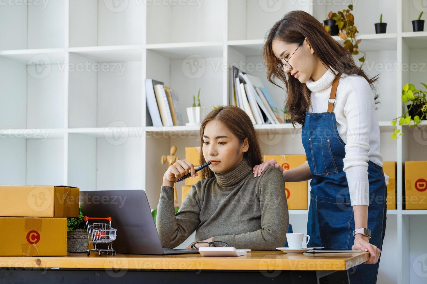 dos mujeres felices que venden productos en línea inician una pequeña empresa usando una computadora portátil y calculan precios y se preparan para el franqueo. foto