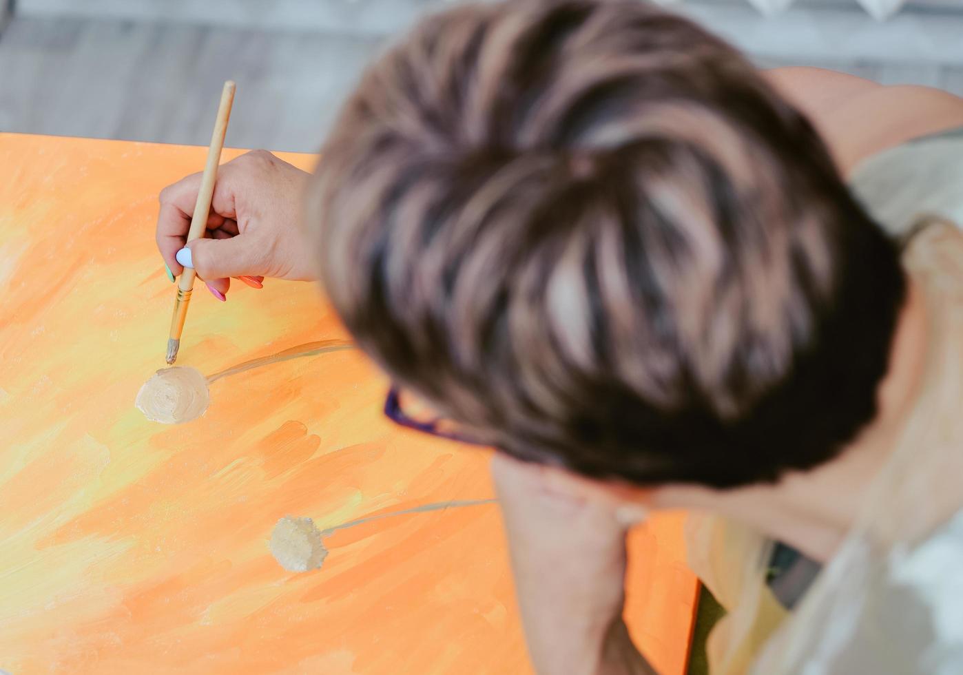senior woman painting with brush, top view. retire lady hobby. recreational activity or therapy for elder people. photo