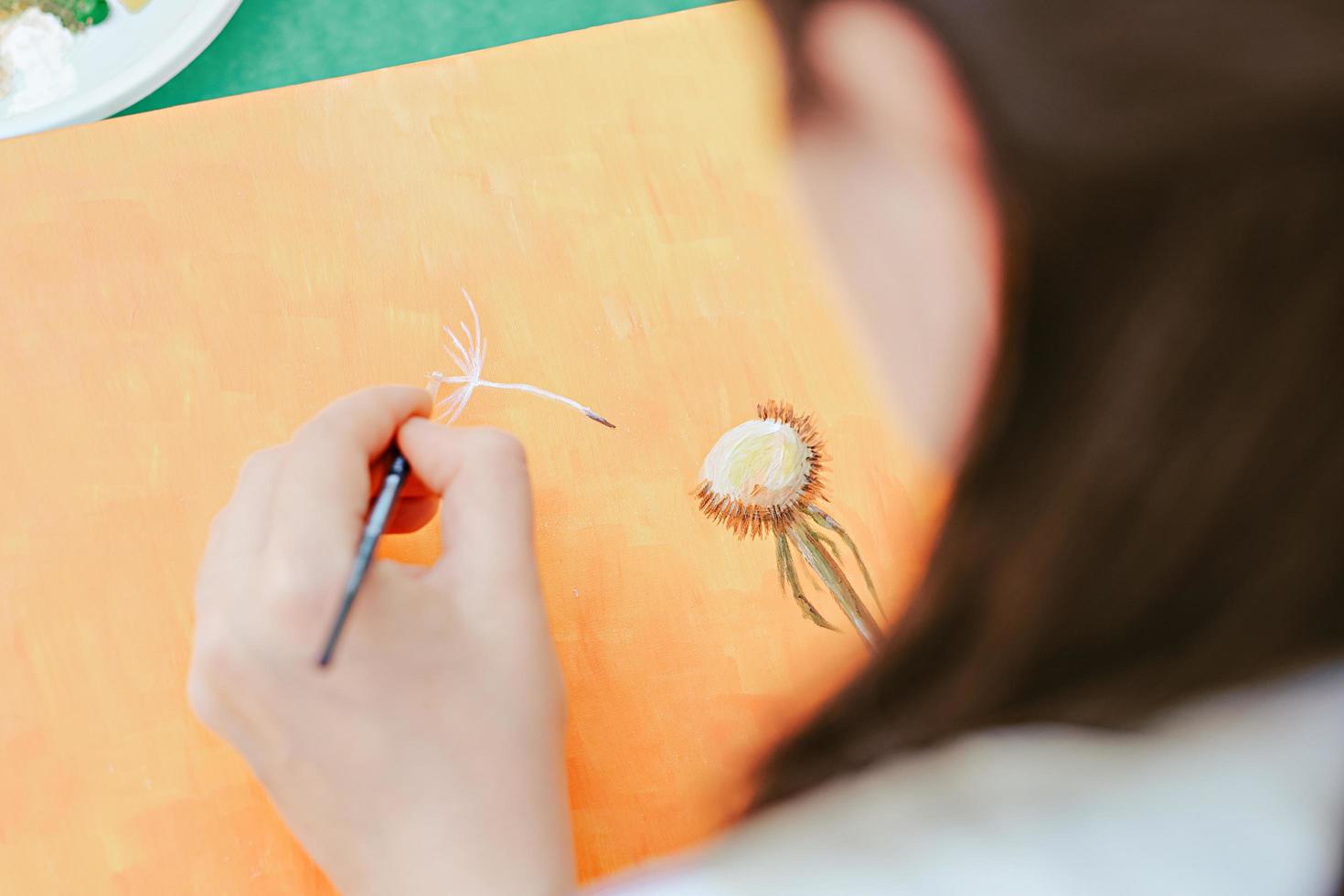 mujer pintando semillas de flores de diente de león con la mano izquierda. ocupación creativa. Día de los zurdos. vista por encima del hombro foto