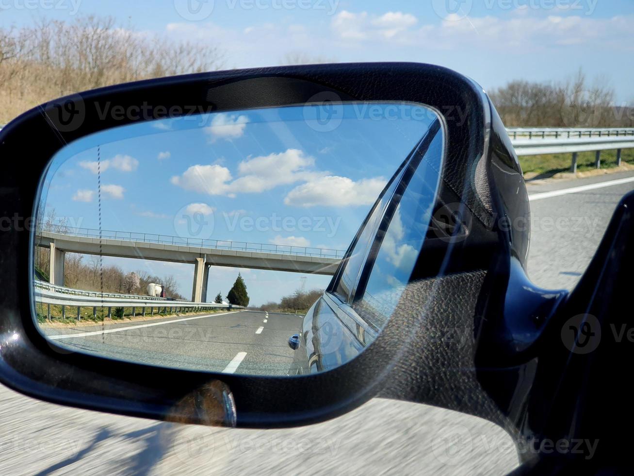 Landscape and road reflection in car rearview black mirror. photo