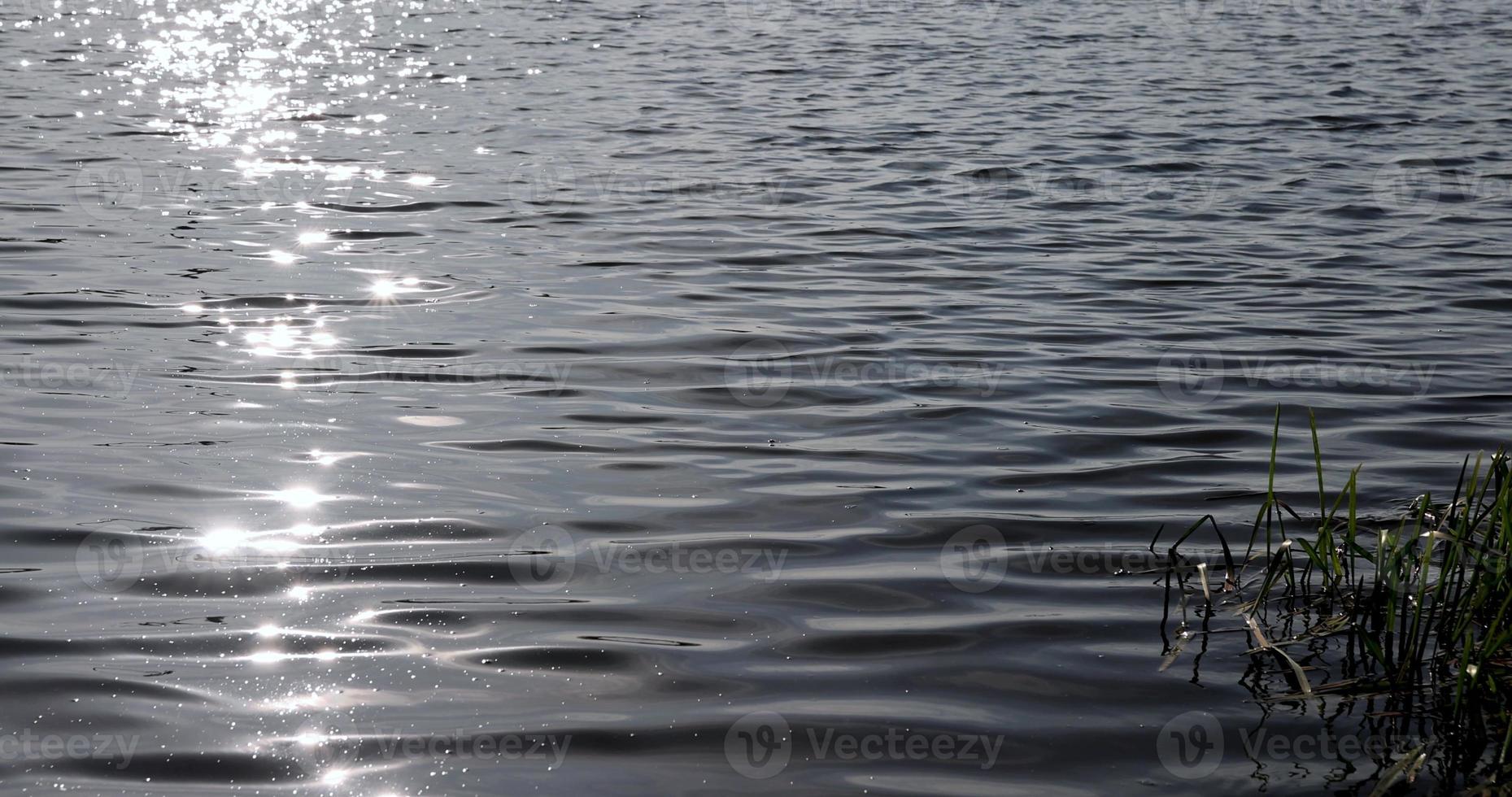 resplandor de la luz del sol en la superficie del agua del lago con pequeñas olas foto