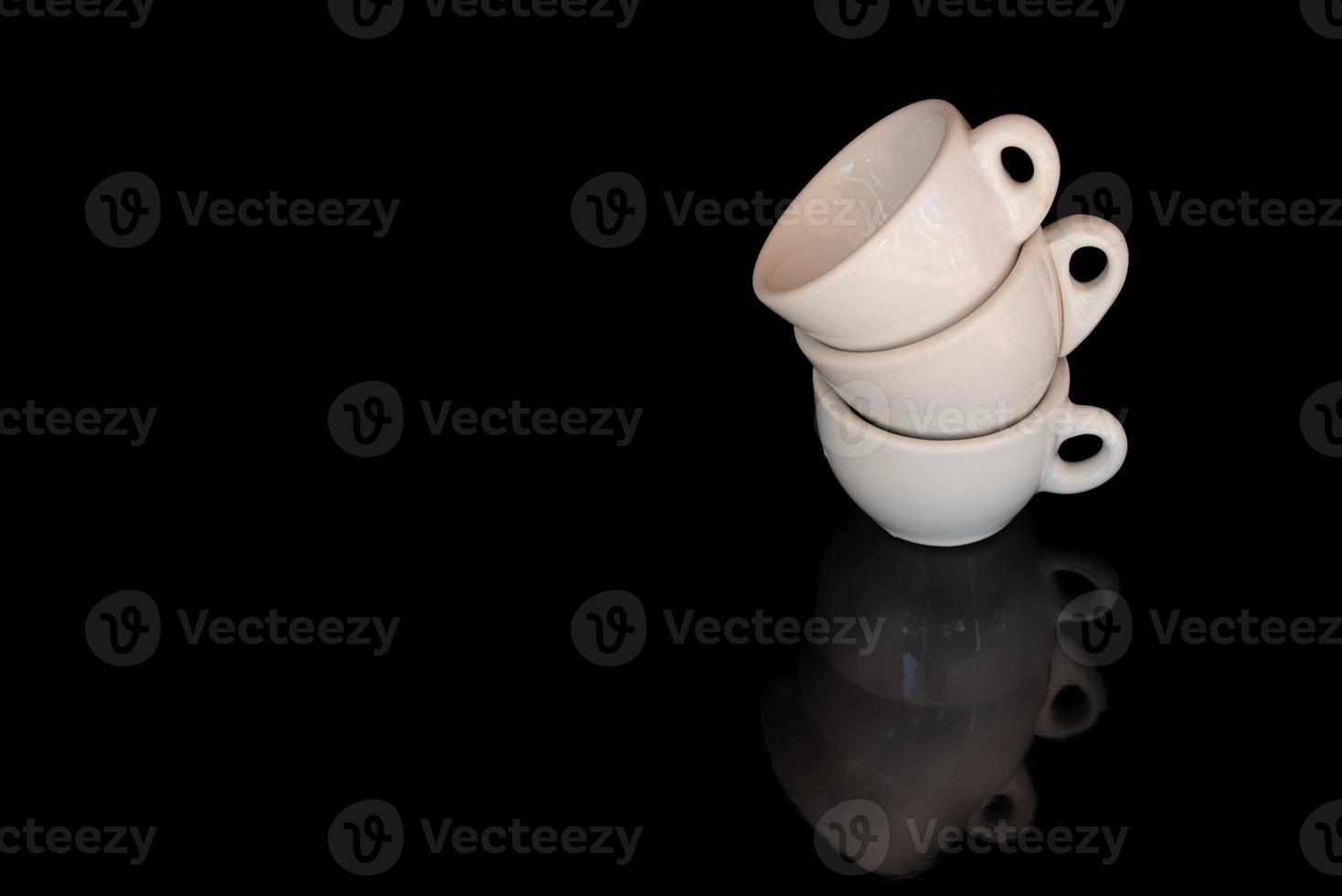 Three white, old espresso cups are stacked on the edge. The background is black. The cups are reflected on the ground. There is space for text. photo