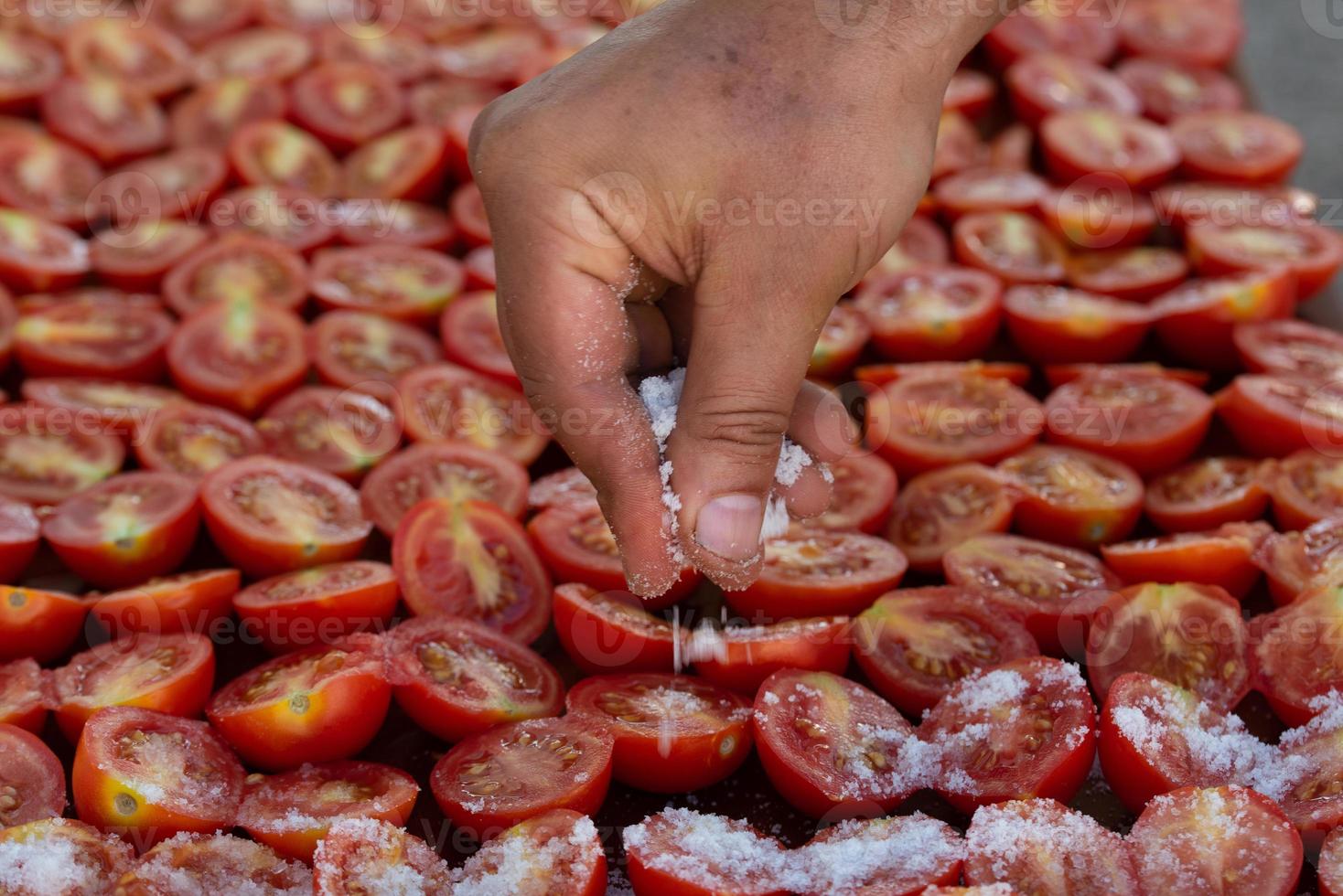 A hand with salt in it sprinkles the salt over tomatoes that are left to dry. photo