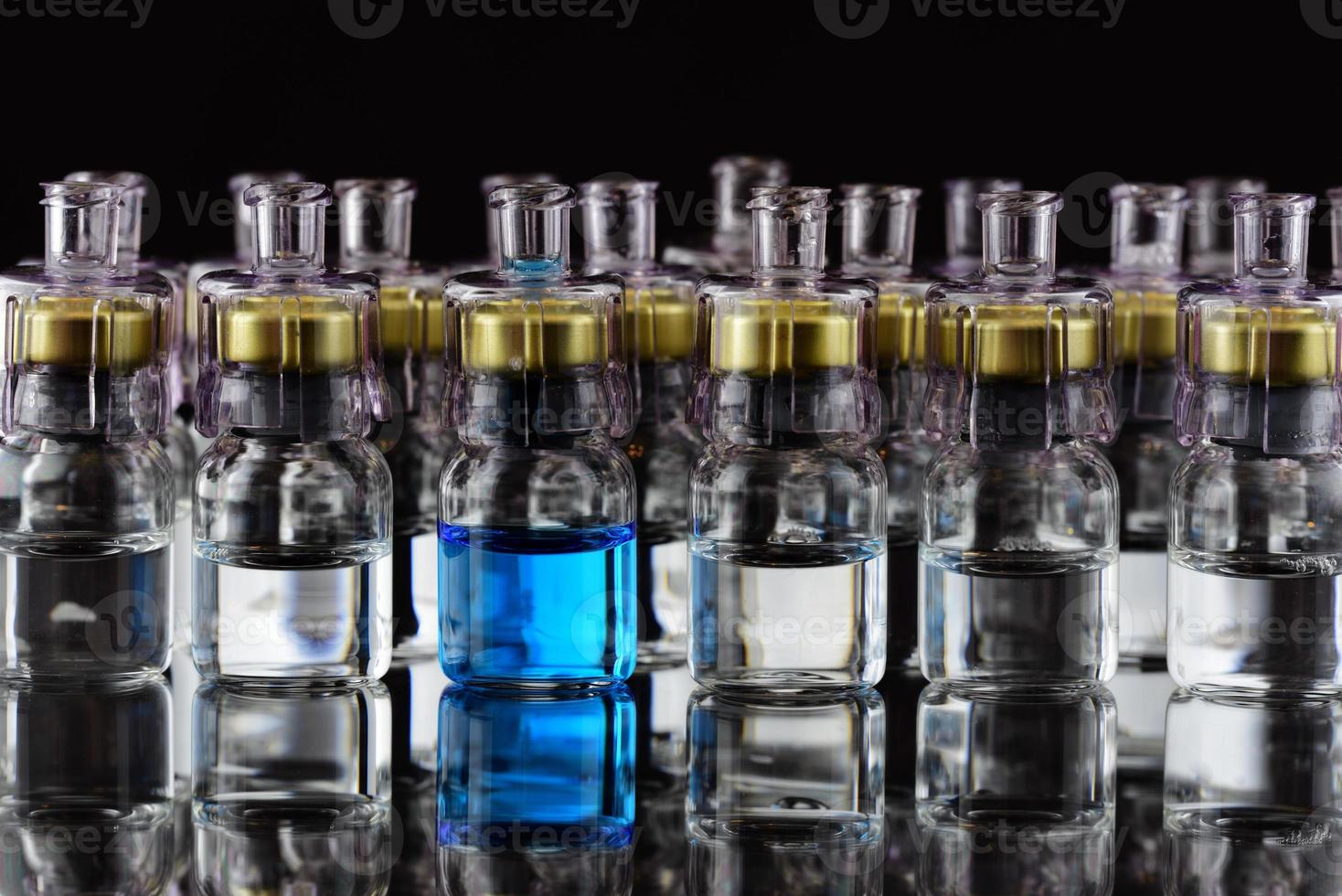 Several glass ampoules are filled with a transparent liquid and stand next to each other against a black background. One ampoule contains blue liquid photo