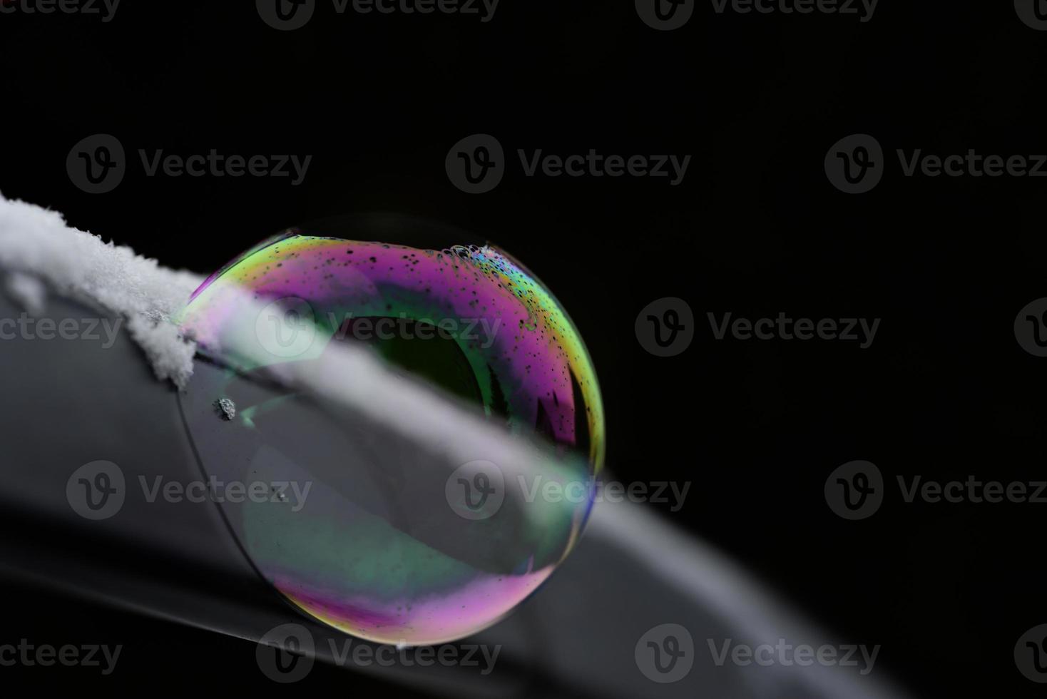 A shimmering soap bubble on a metal arch against a dark background in winter photo