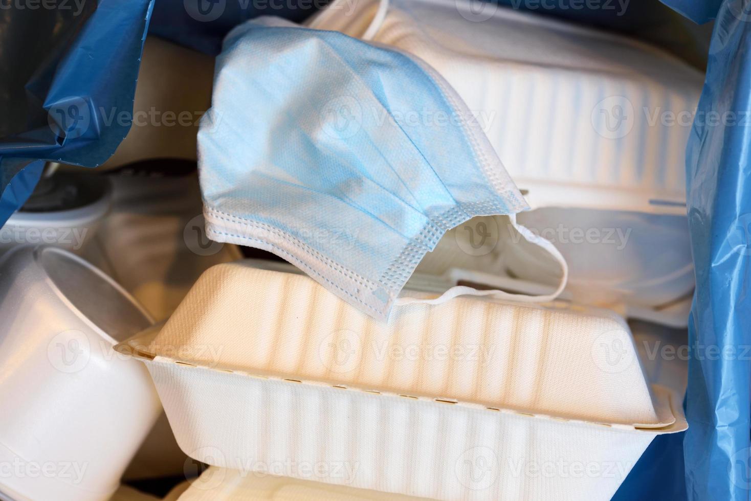 Used disposable styrofoam dishes and a used face mask lie in a plastic garbage bag photo