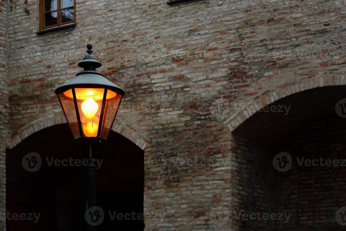 a glowing lantern stands in front of old and historic brick walls at dusk in the evening photo