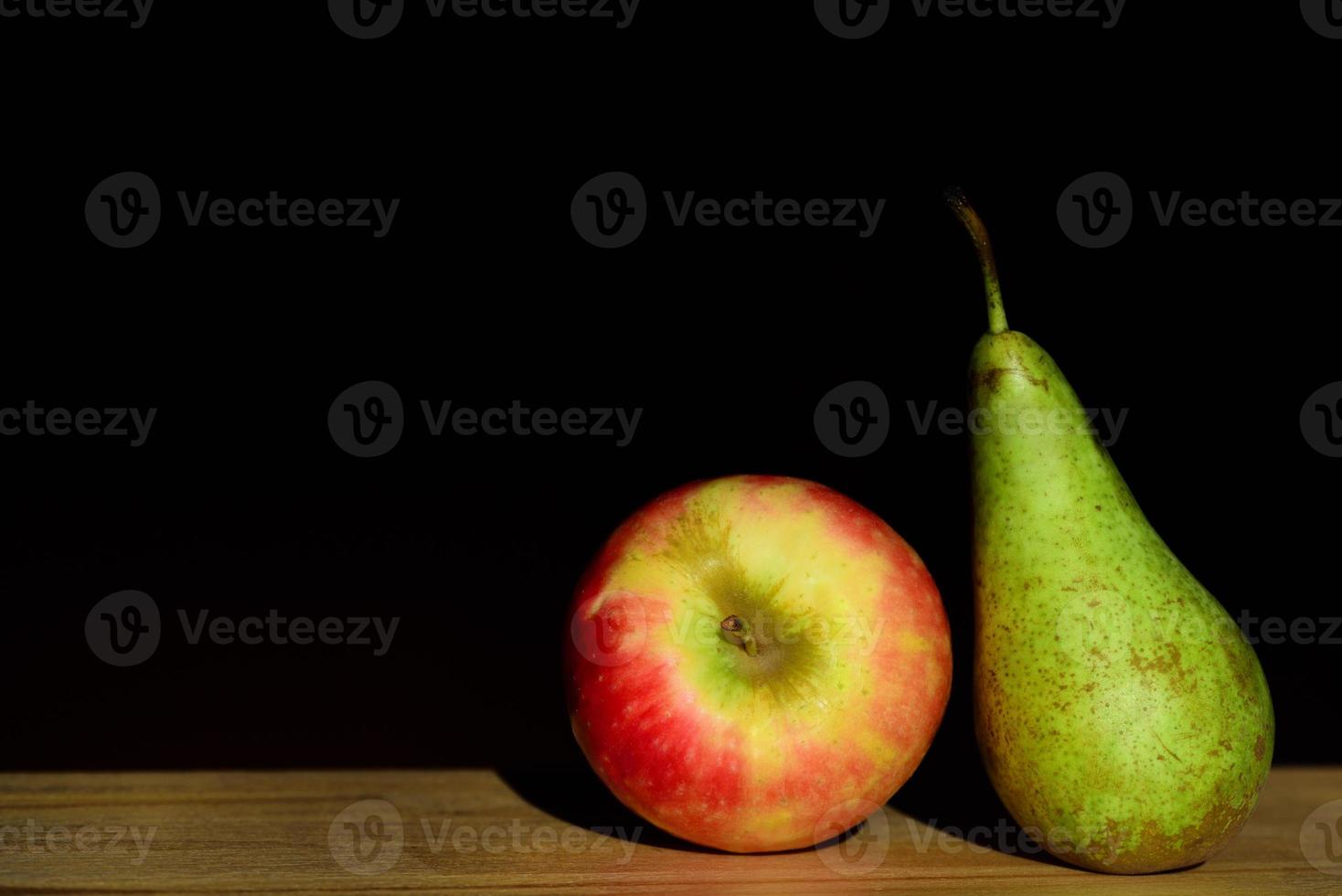 An apple and a pear lie next to each other on a table against a dark background photo