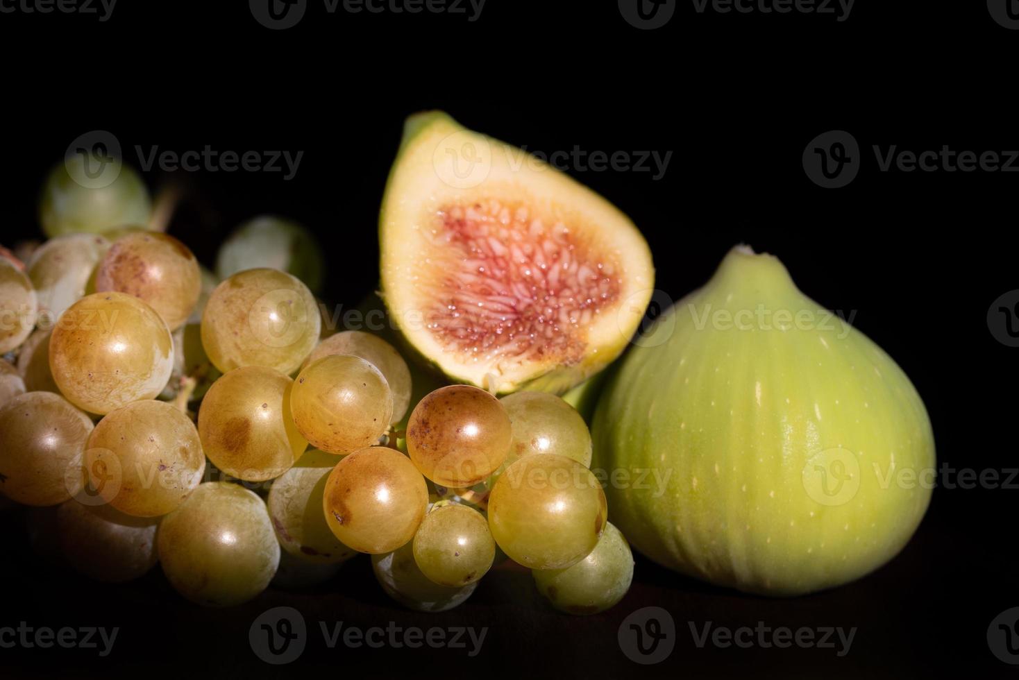 Sweet ripe grapes and green figs lie on a table against a dark background photo
