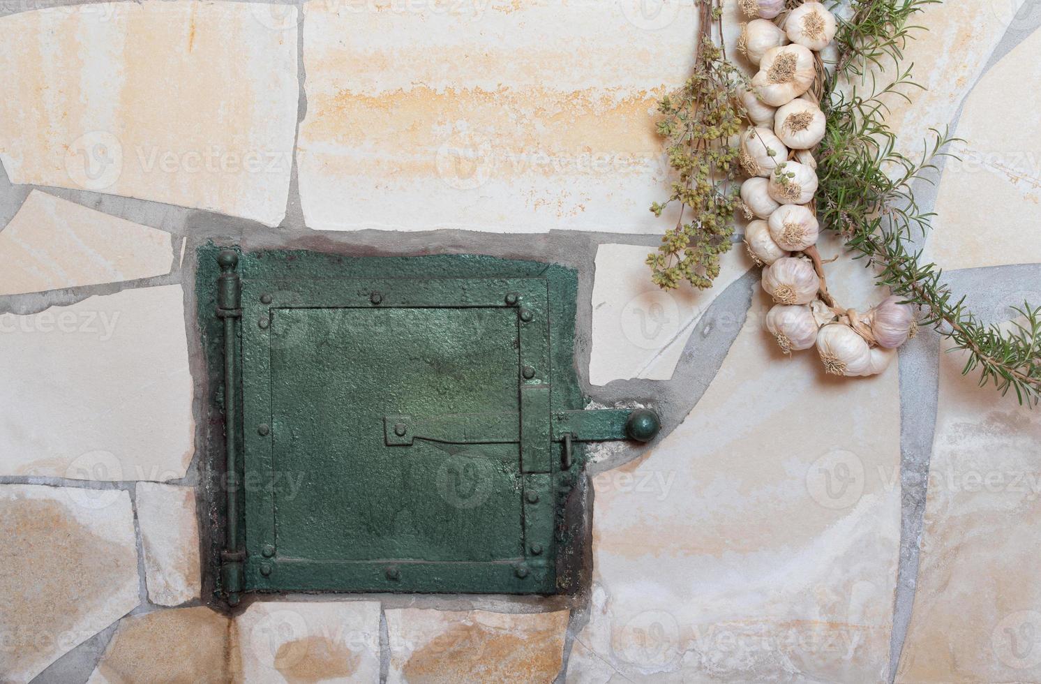 Background and closeup of a traditional oven with an oven door. Herbs and garlic hang down on the sides photo