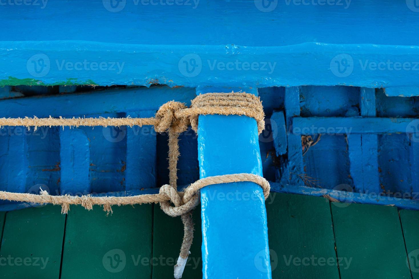 Close up, detail shot and background of an old wooden fishing boat painted blue and green paint. You see a bench to which two ropes are attached. photo