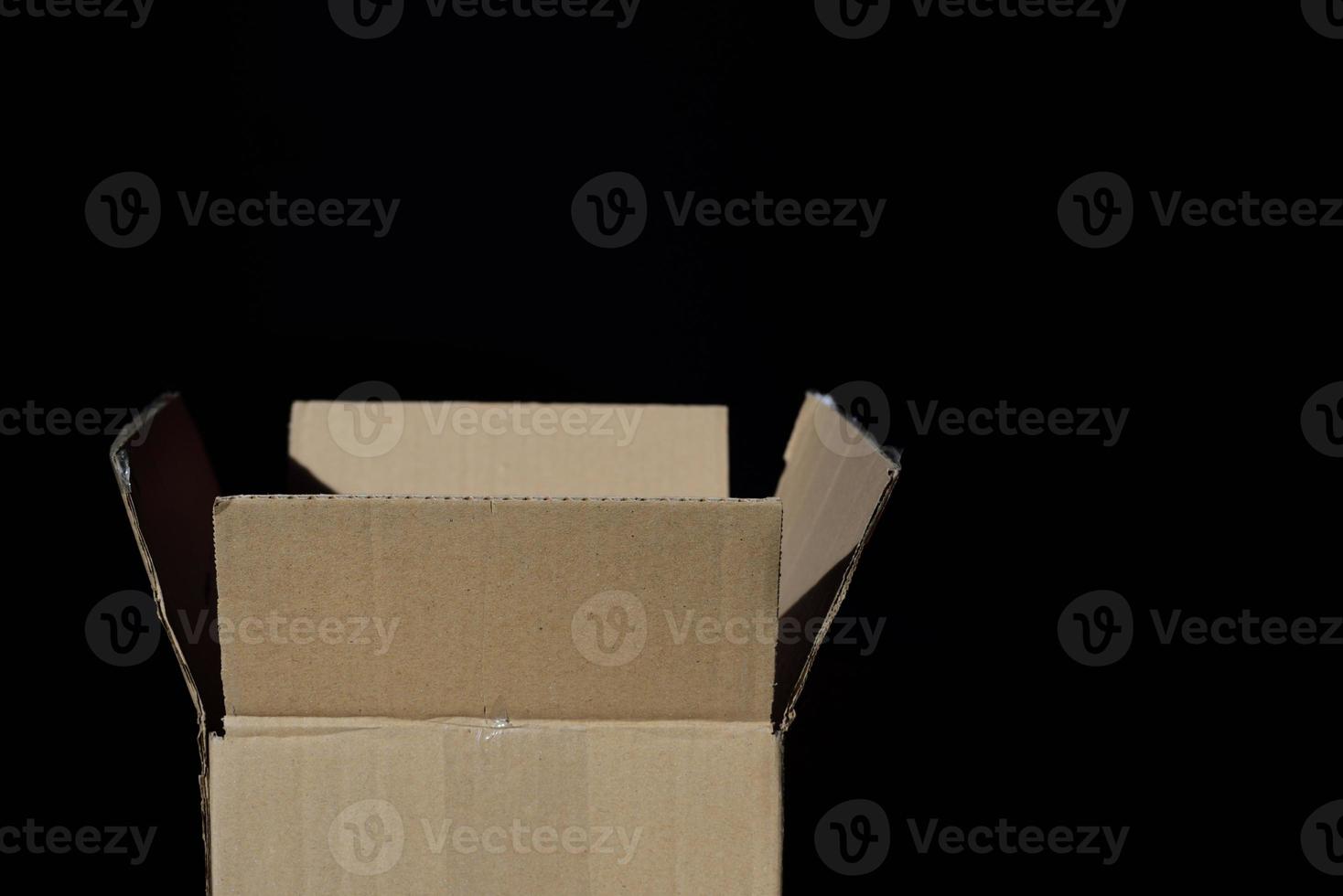 An open and empty cardboard box stands in front of a dark background photo