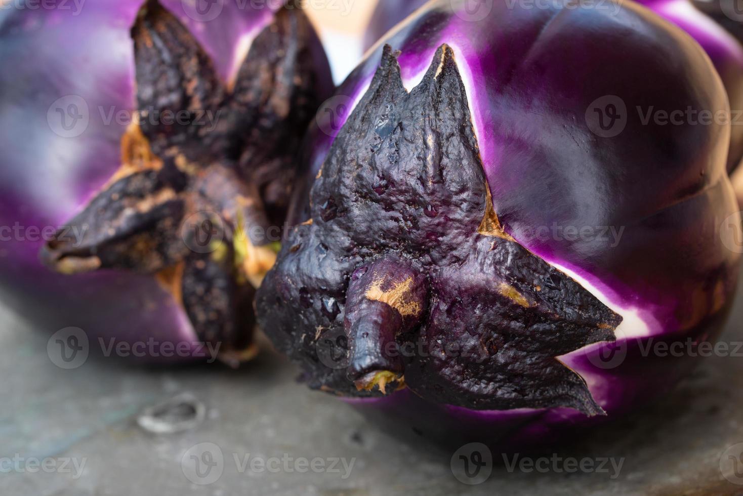 Close up of two round purple aubergines lying side by side on an old gray copper plate. photo