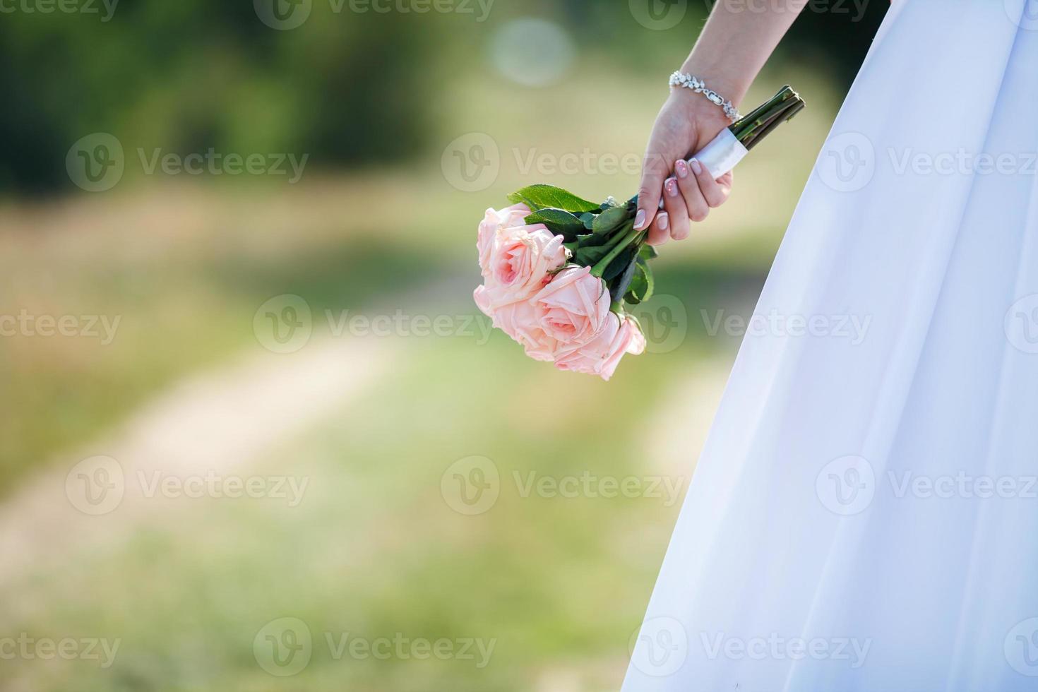 bride in a white dress with a wedding bouquet of white and pink roses in park photo