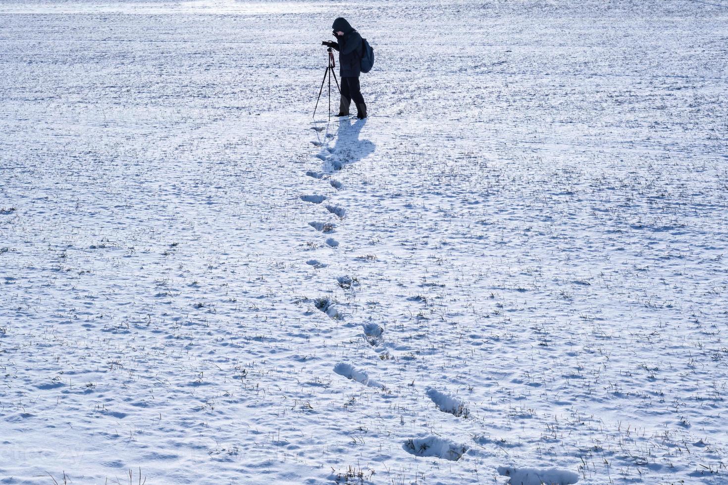 fotógrafo con un trípode en un campo nevado toma fotos del paisaje, huellas en la nieve