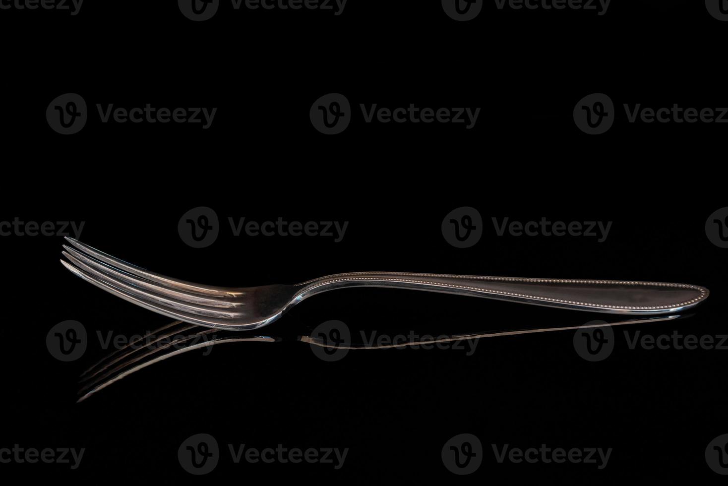 Close-up of an empty old fork with long tines reflected against a dark background. photo