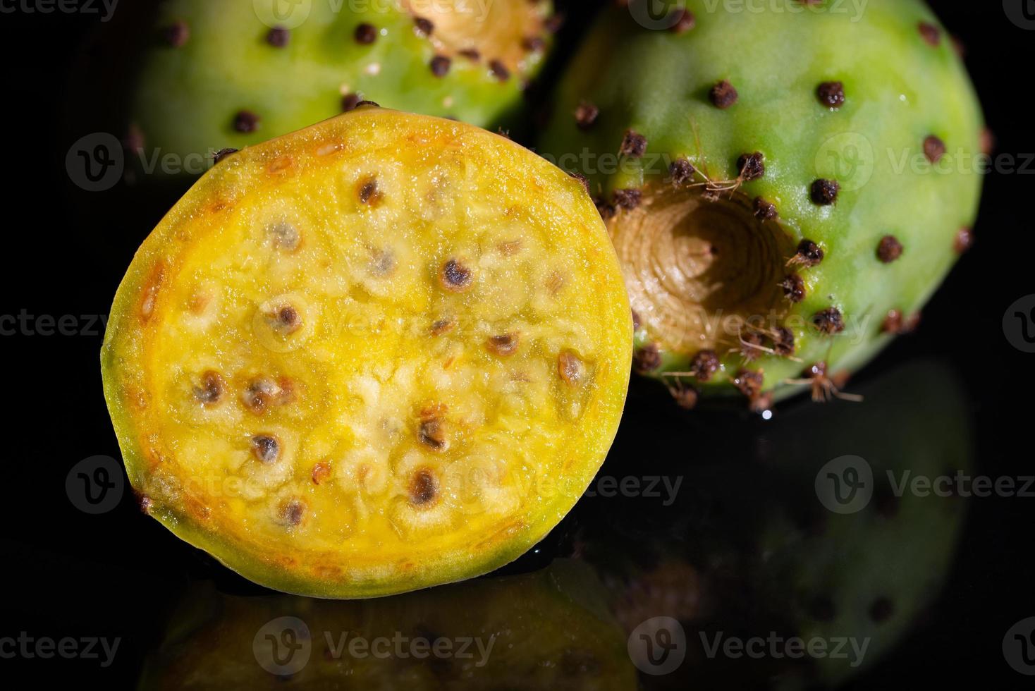 Close-up of fresh prickly pears lying against a dark background and reflected on the base. A cactus fruit is cut open. photo