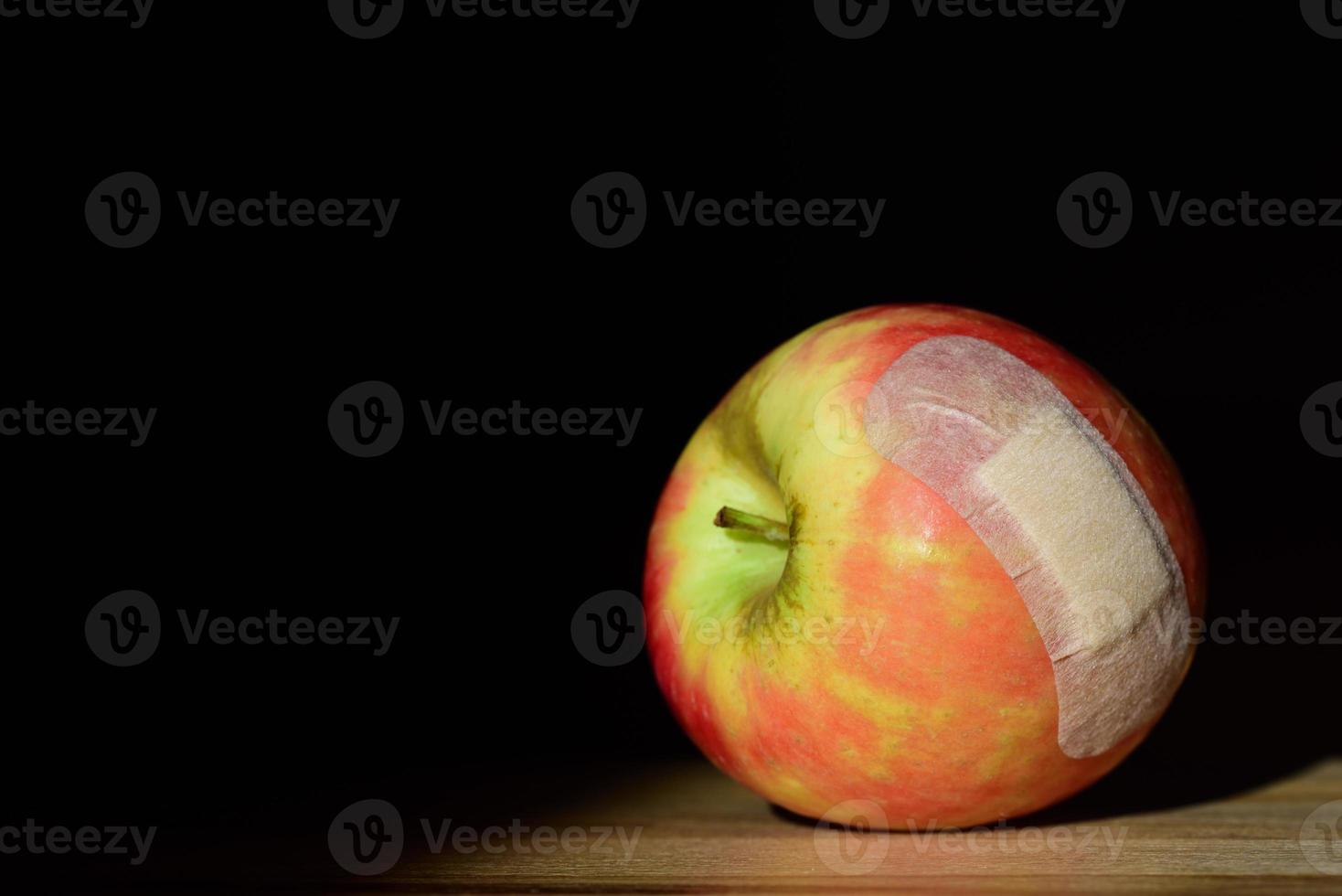 An apple lies on a table in front of a dark background and is covered with a plaster photo