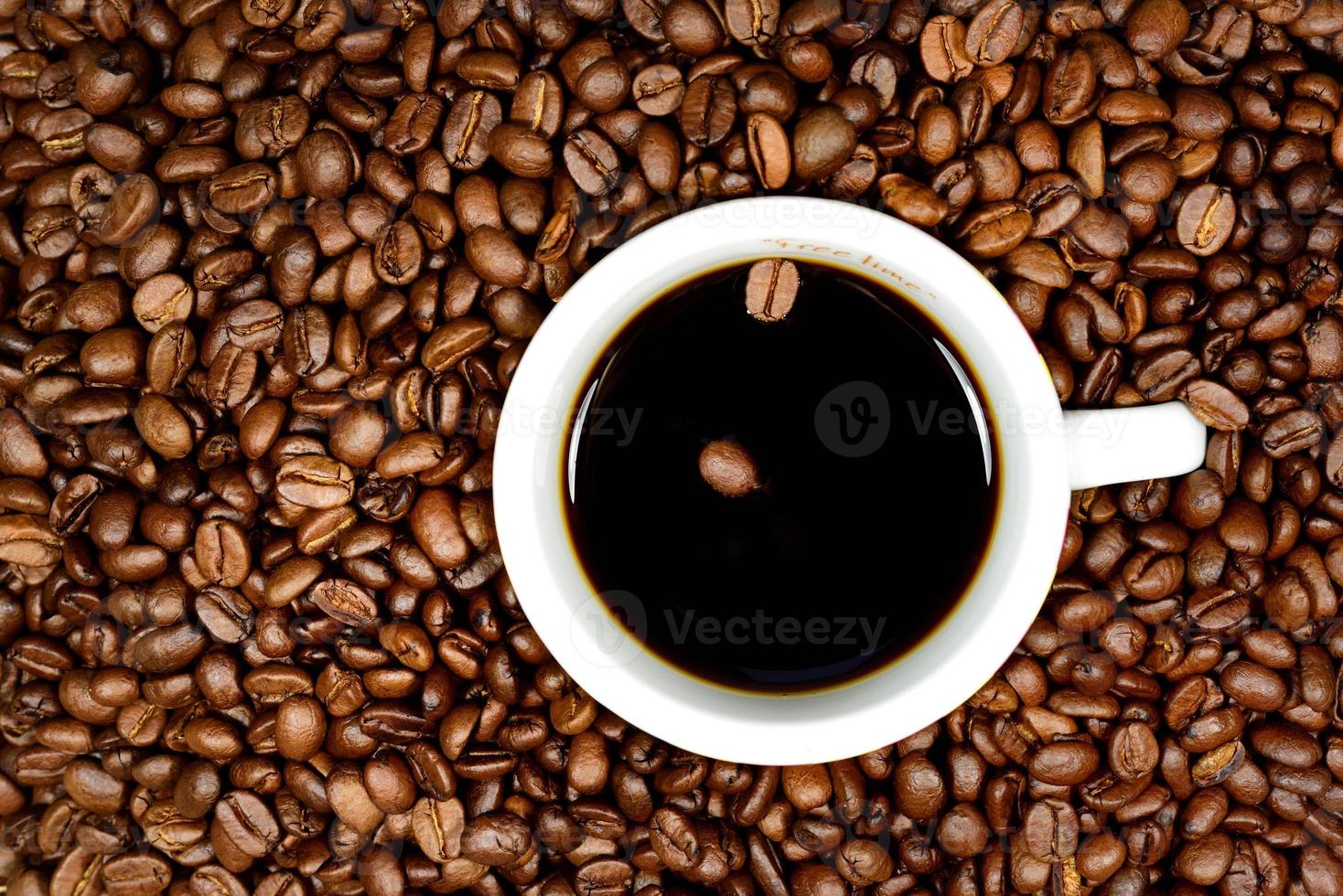 A cup of black coffee with two coffee beans floating in it stands against the background of many brown coffee beans photo