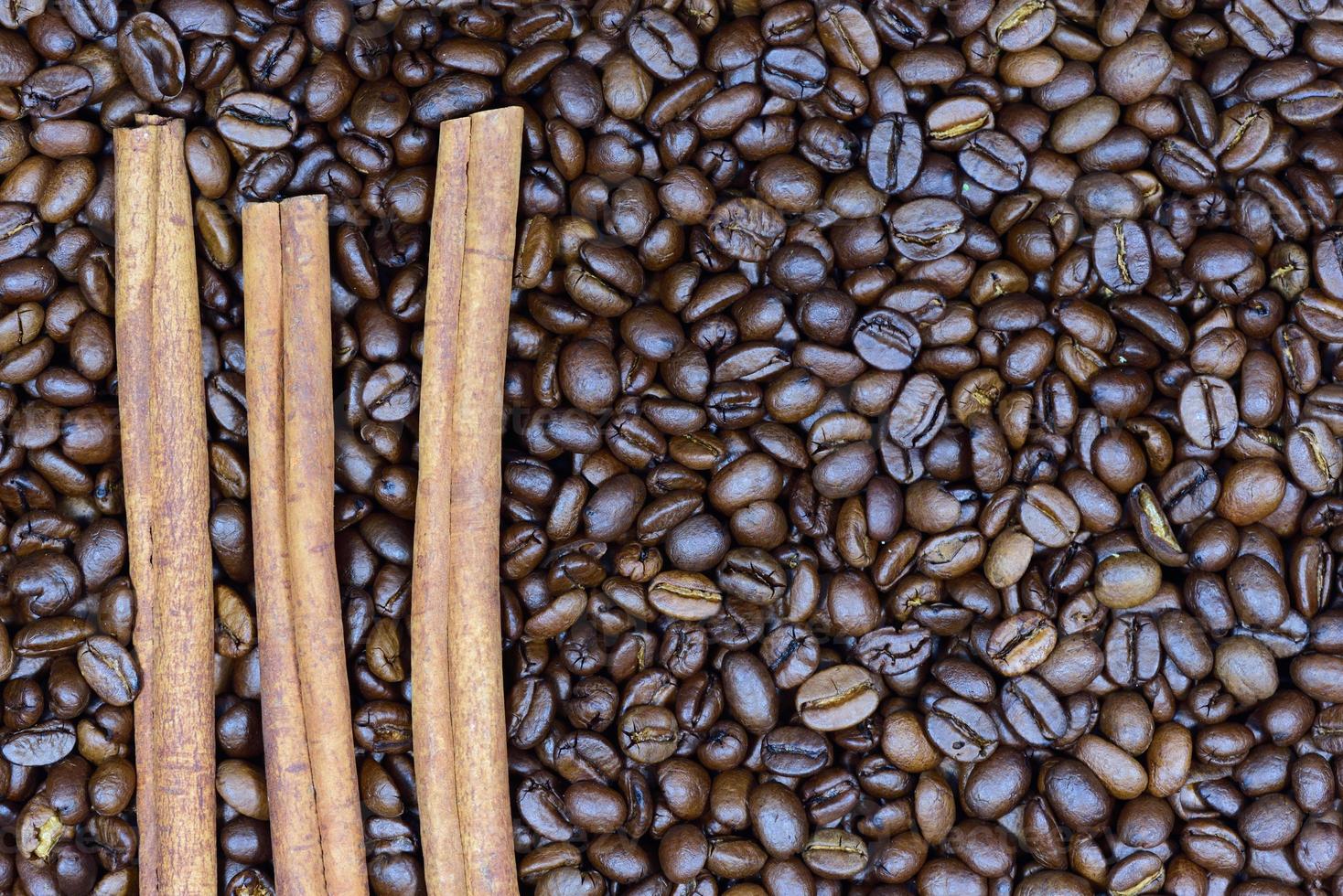 Three brown cinnamon sticks lie on top of brown roasted coffee beans photo