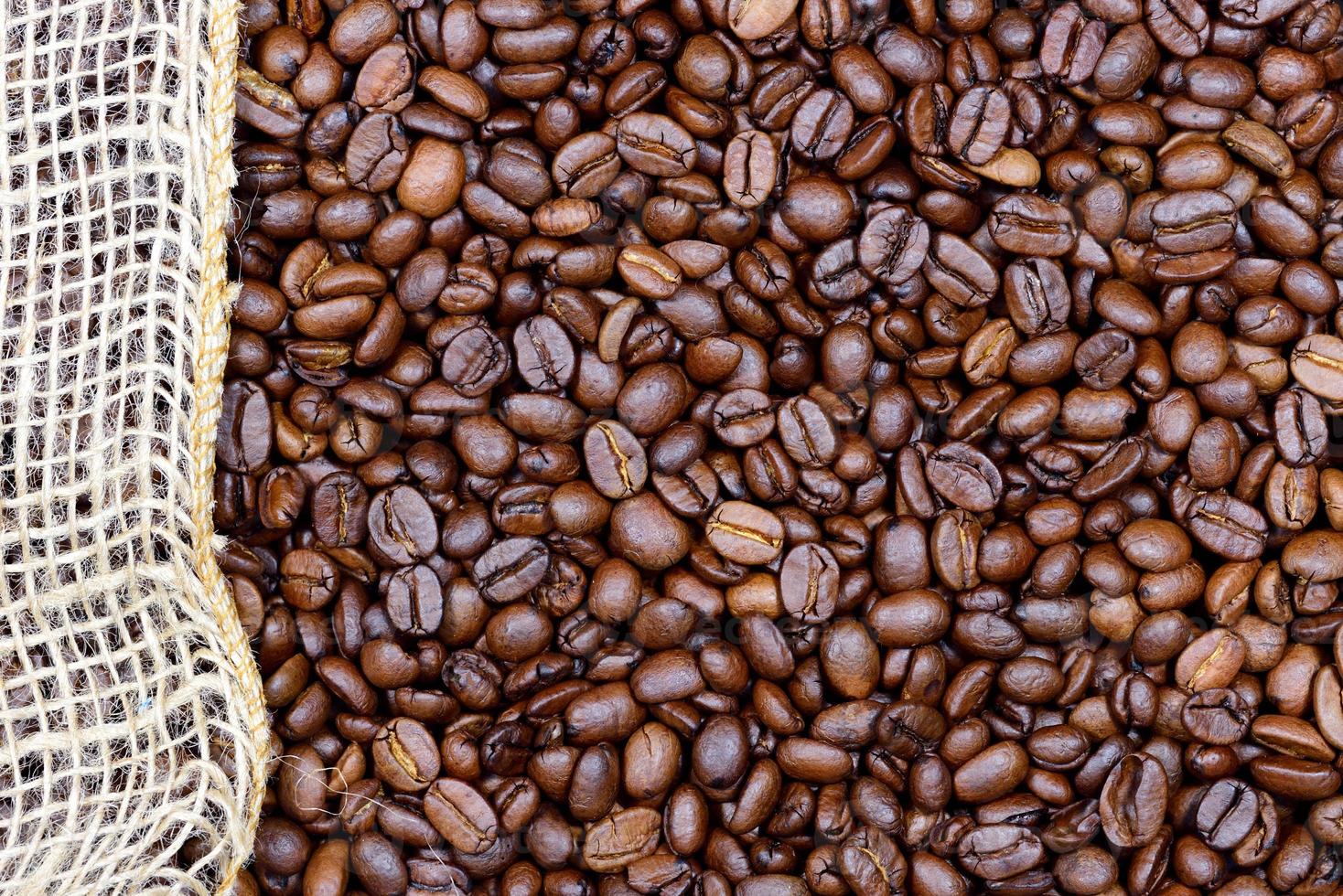 Background, close-up and texture of roasted coffee beans with a piece of jute running along the edge photo