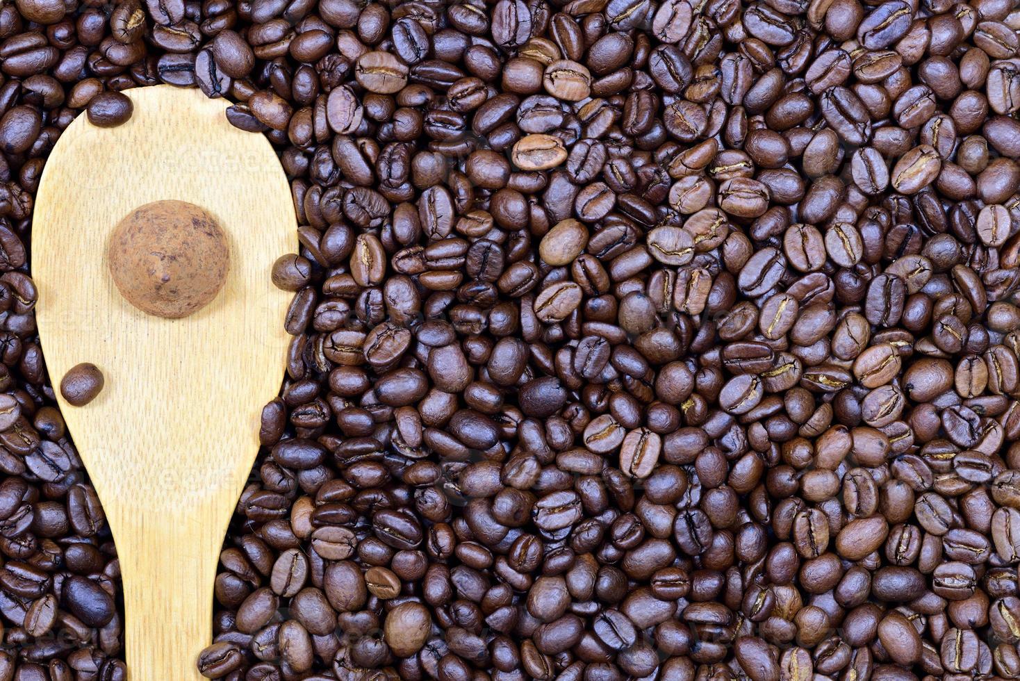 Close up, texture and background of roasted fresh coffee beans on which a wooden spoon lies and a chocolate truffle praline on top photo