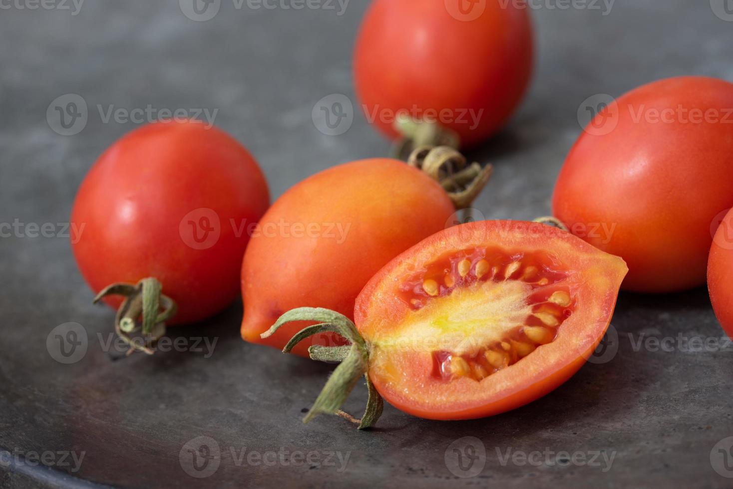 On an old, gray copper plate lies a group of small red tomatoes. The tomatoes are pointed at the front and come from Sicily. A tomato is cut open. photo