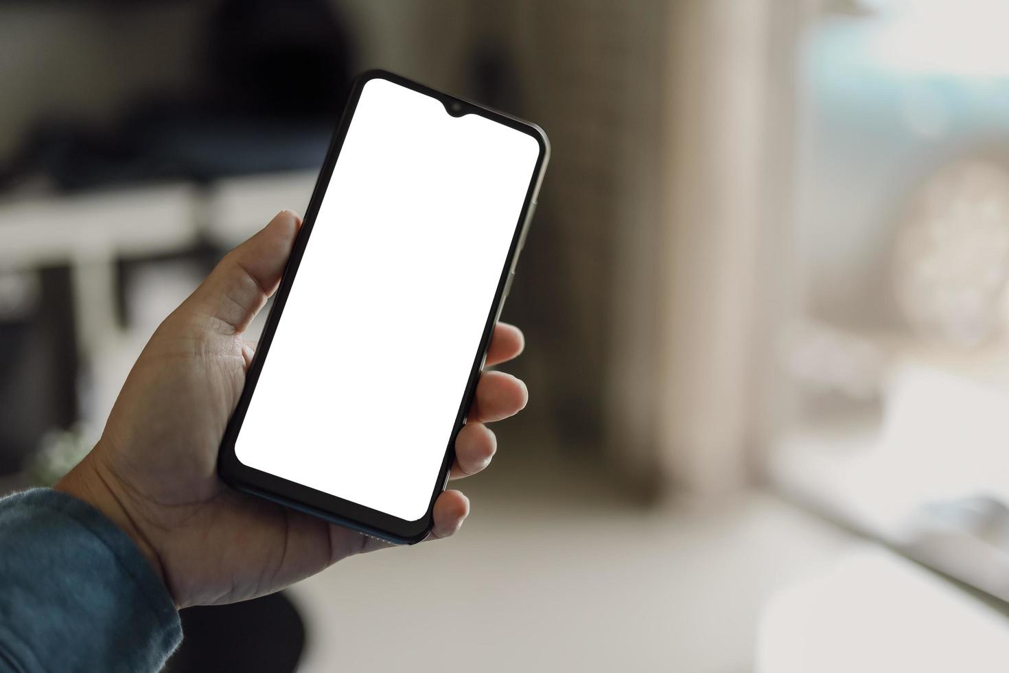 Mockup image of a man holding black mobile phone with blank white screen. In living room at home. photo