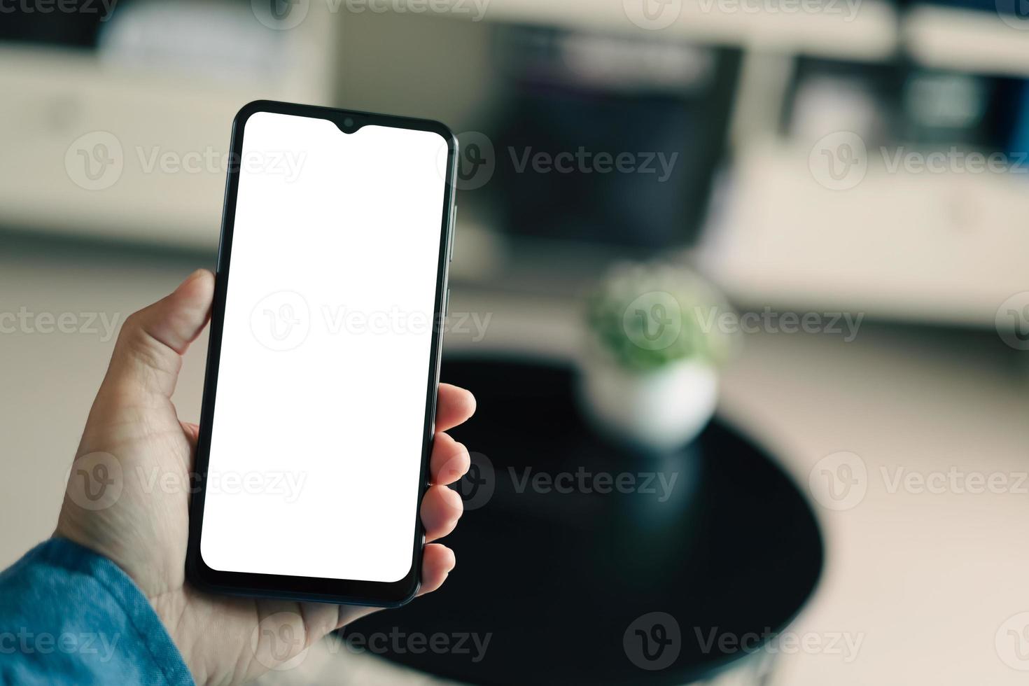 Mockup image of a man holding black mobile phone with blank white screen. In living room at home. photo