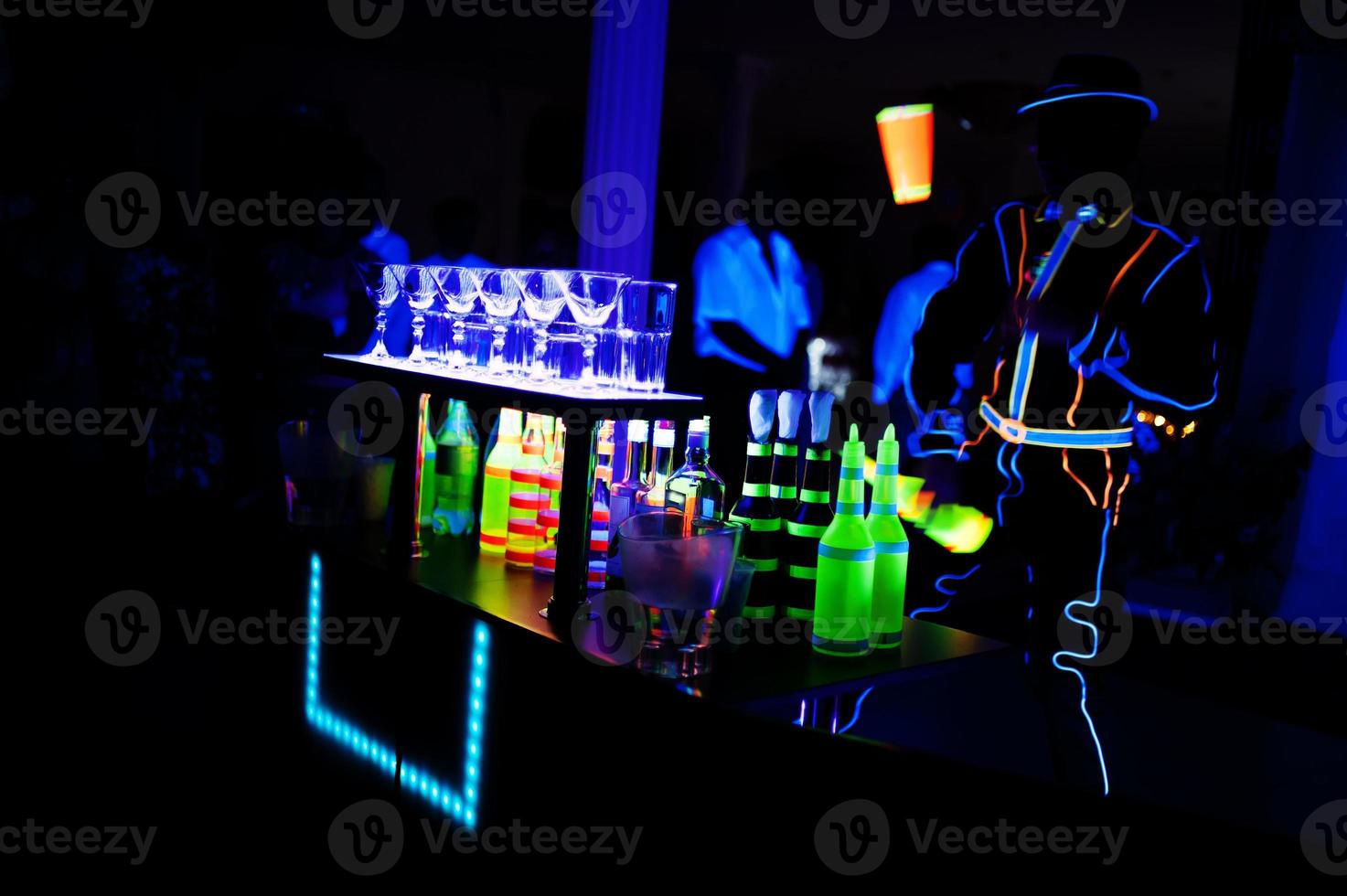 Professional barman and led light show. Silhouette of modern bartender shaking drink at night cocktail bar. photo