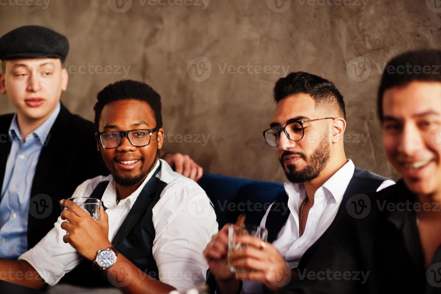 Group of handsome retro well-dressed man gangsters spend time at club, sitting and drinking whiskey. Multiethnic male bachelor mafia party in restaurant. photo