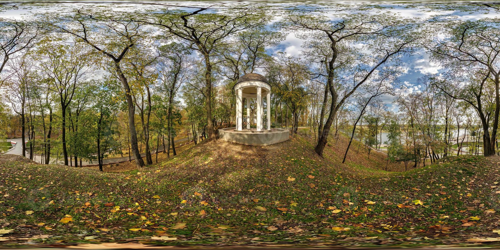 full seamless spherical hdri panorama 360 degrees view of autumn forest or park with bright sun shining through trees near concrete gazebo with columns in equirectangular projection, VR AR content photo