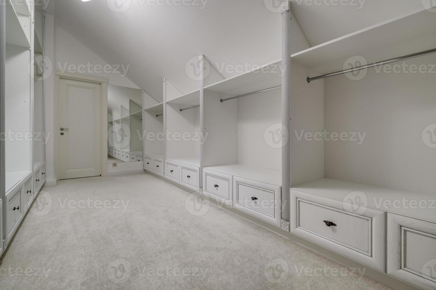 rows of shelves and clothes hangers in empty big wardrobe room in modern apartment or hotel photo