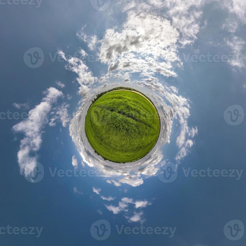 green tiny planet in blue sky with sun and beautiful clouds. Transformation of spherical panorama 360 degrees. Spherical abstract aerial view. Curvature of space. photo