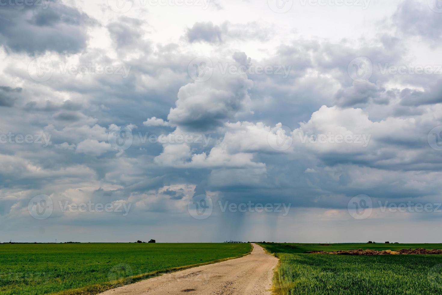 landscape with dark sky with rain clouds before storm in green field with gravel road. thunderstorm front photo